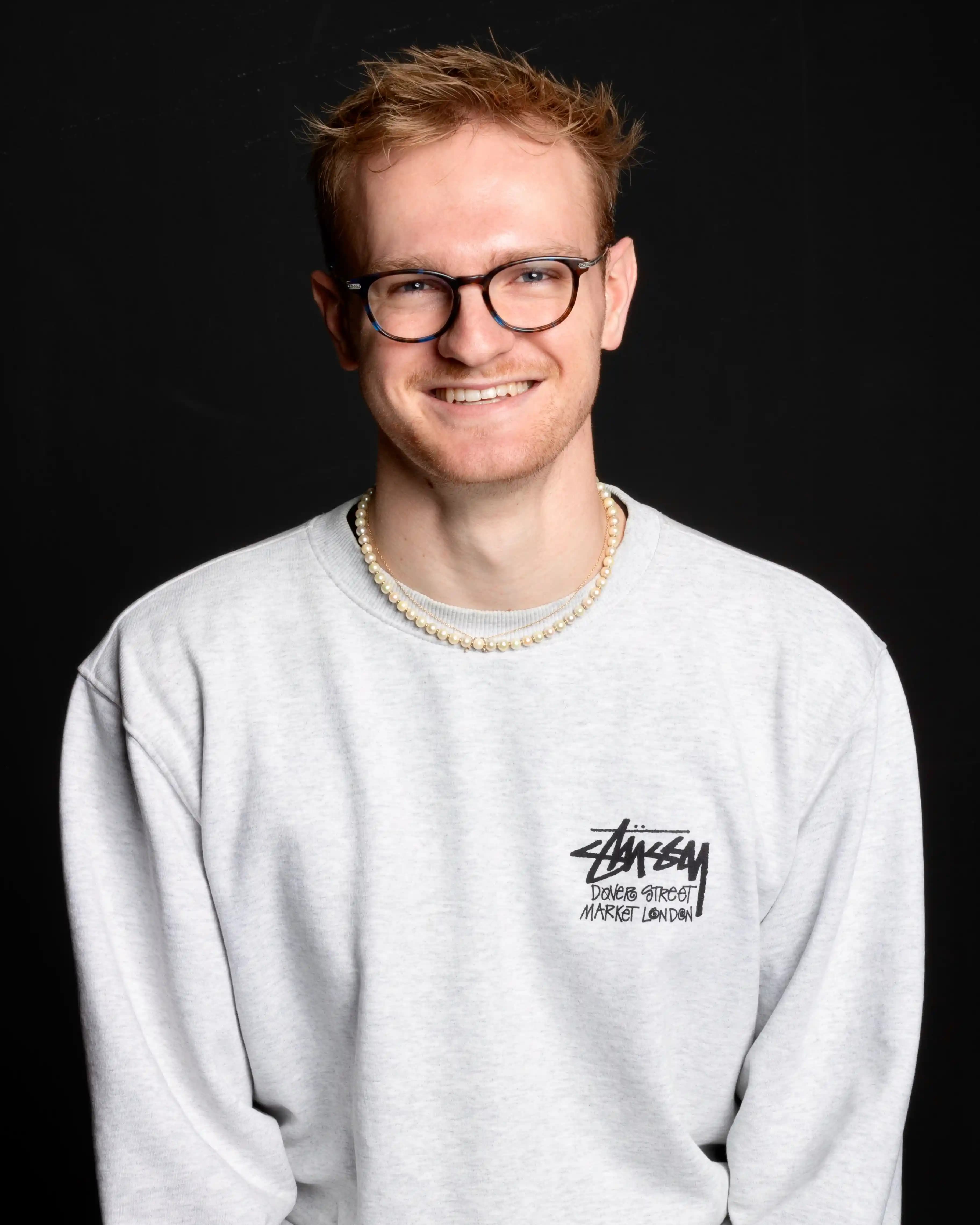 Noah is sat wearing a grey jumper in front of a black background