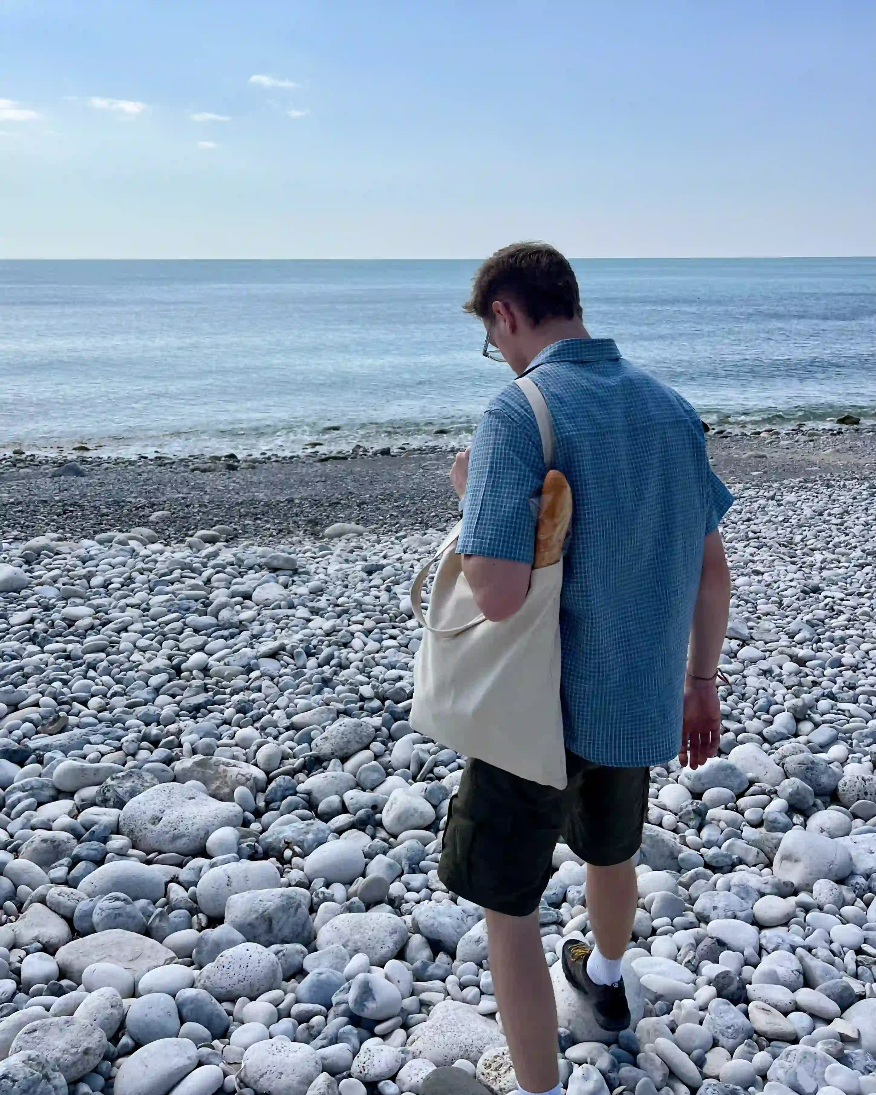 A photo of the sea and stony beach with Noah facing away from the camera