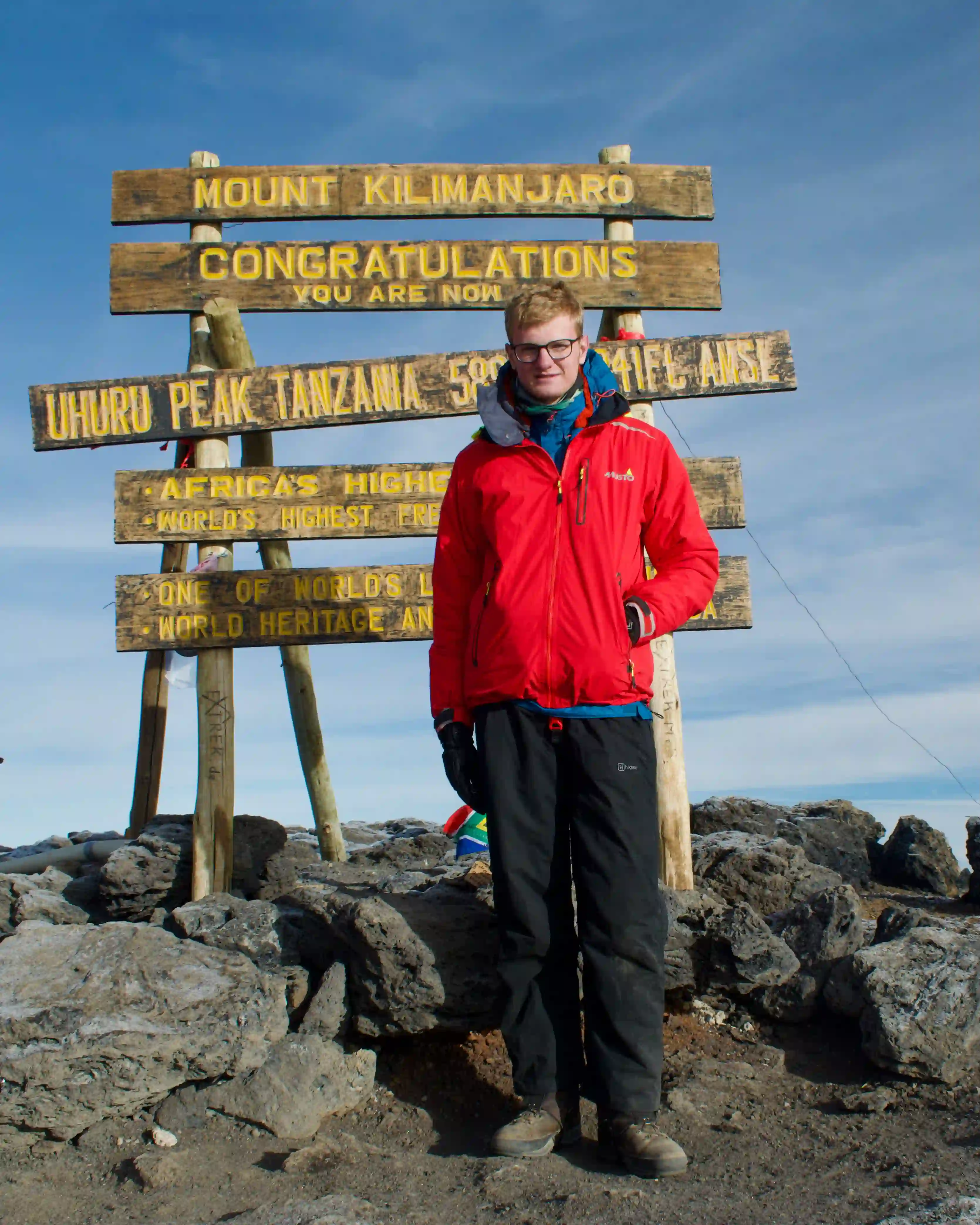 Noah stood at the peak of Mount Kilimanjaro, in front of a wooden sign