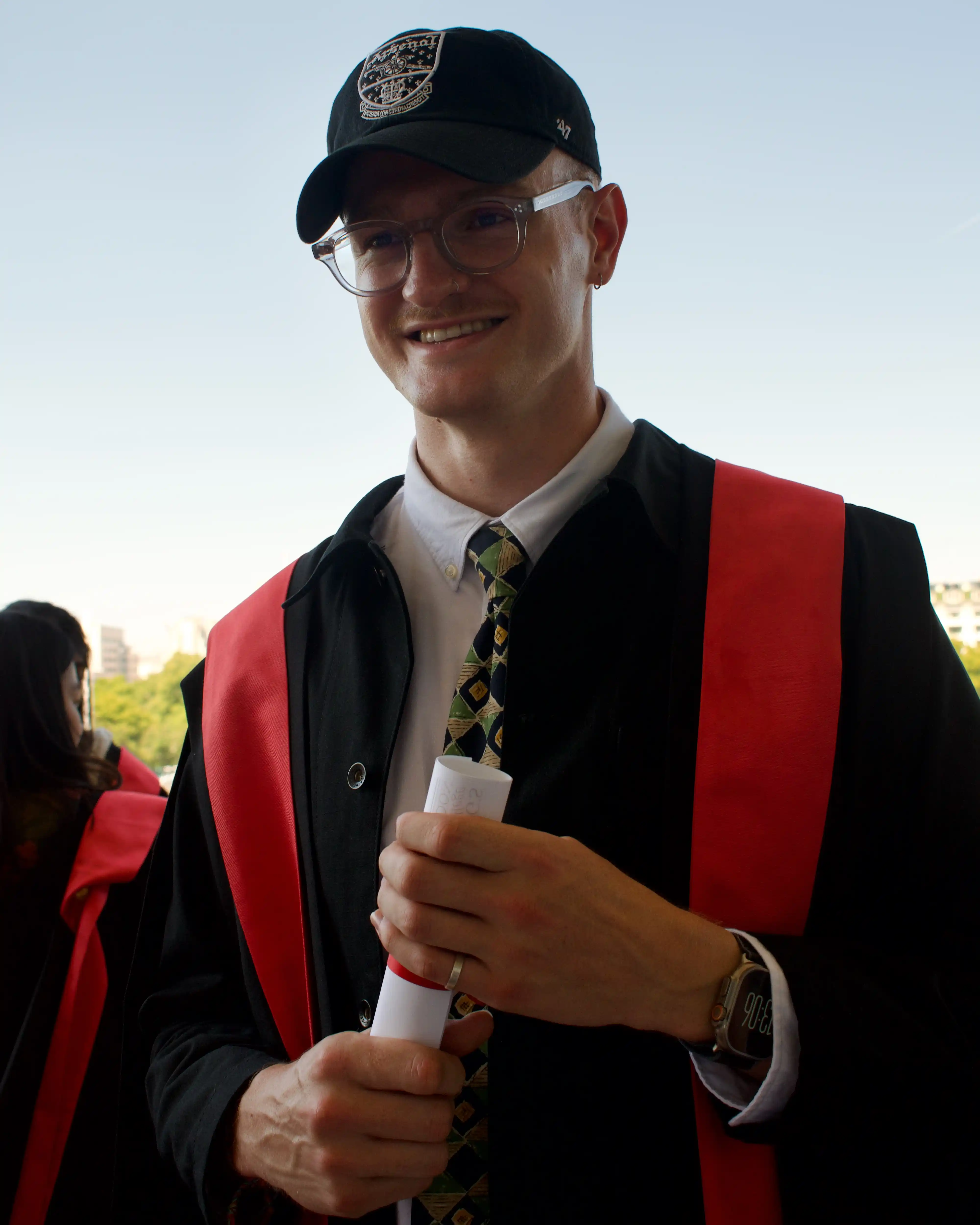 Noah smiling off to the side while wearing an Arsenal Football cap and holding his degree scroll