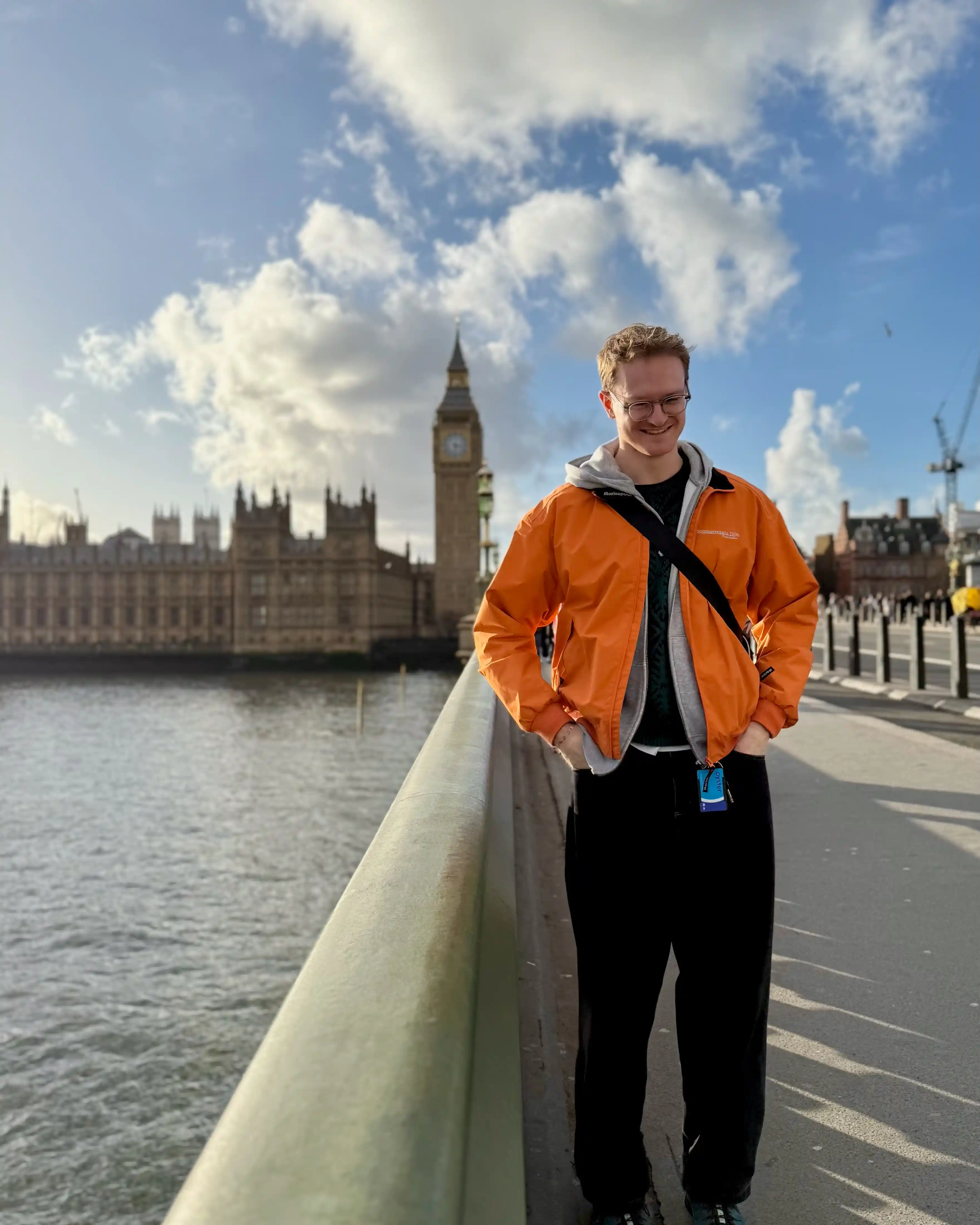 Noah stood on westminster Bridge wearing an orange jacket with Big Ben in the background